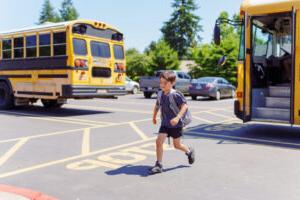 An elementary age boy walks across the street after riding the school bus.
